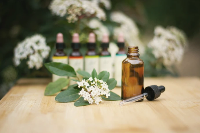 a bottle of essential oils sitting on a table next to a bunch of flowers