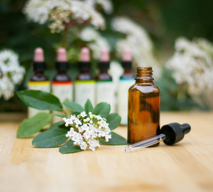 a bottle of essential oils sitting on a table next to a bunch of flowers